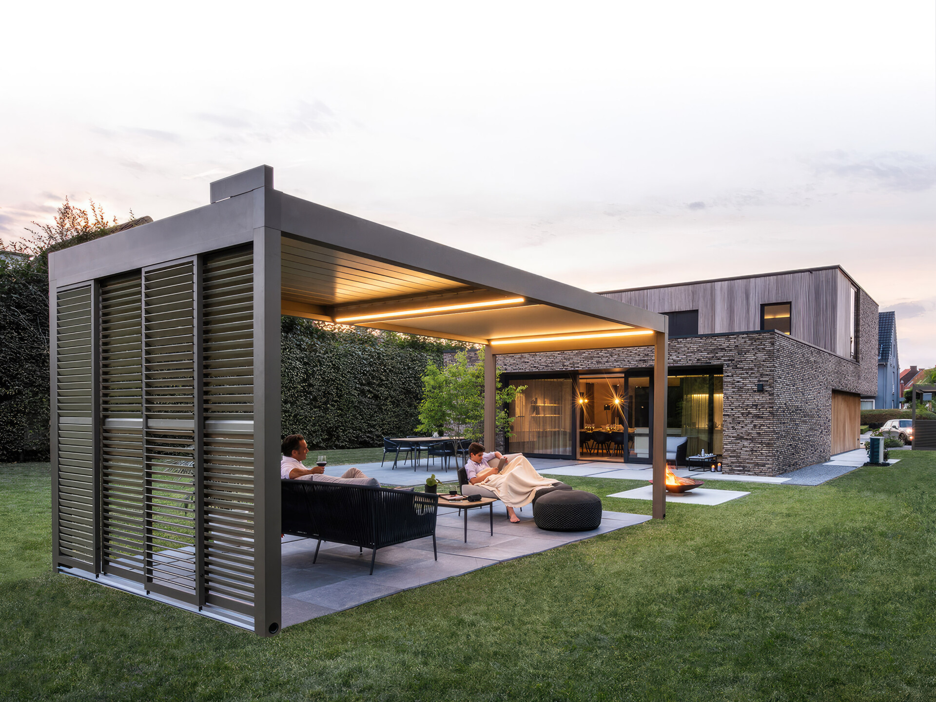 A pergola with integrated lighting over a patio furnished with outdoor seating, and a well-manicured lawn complementing the sleek architectural design.